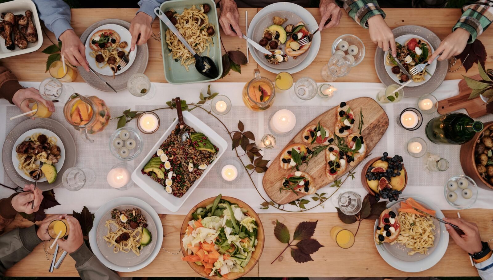 Overhead shot of a vibrant dining table setup with pasta, salads, and decorative candles, capturing a festive gathering.
