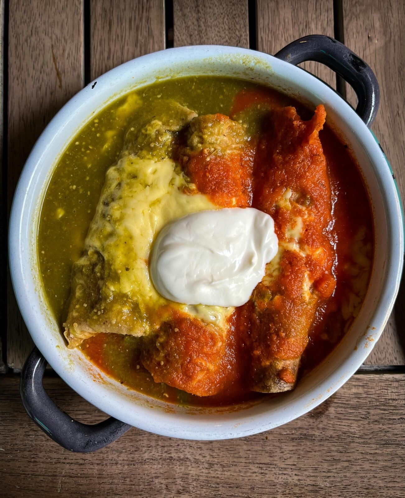 Delicious Mexican enchiladas topped with red and green salsa, and sour cream.