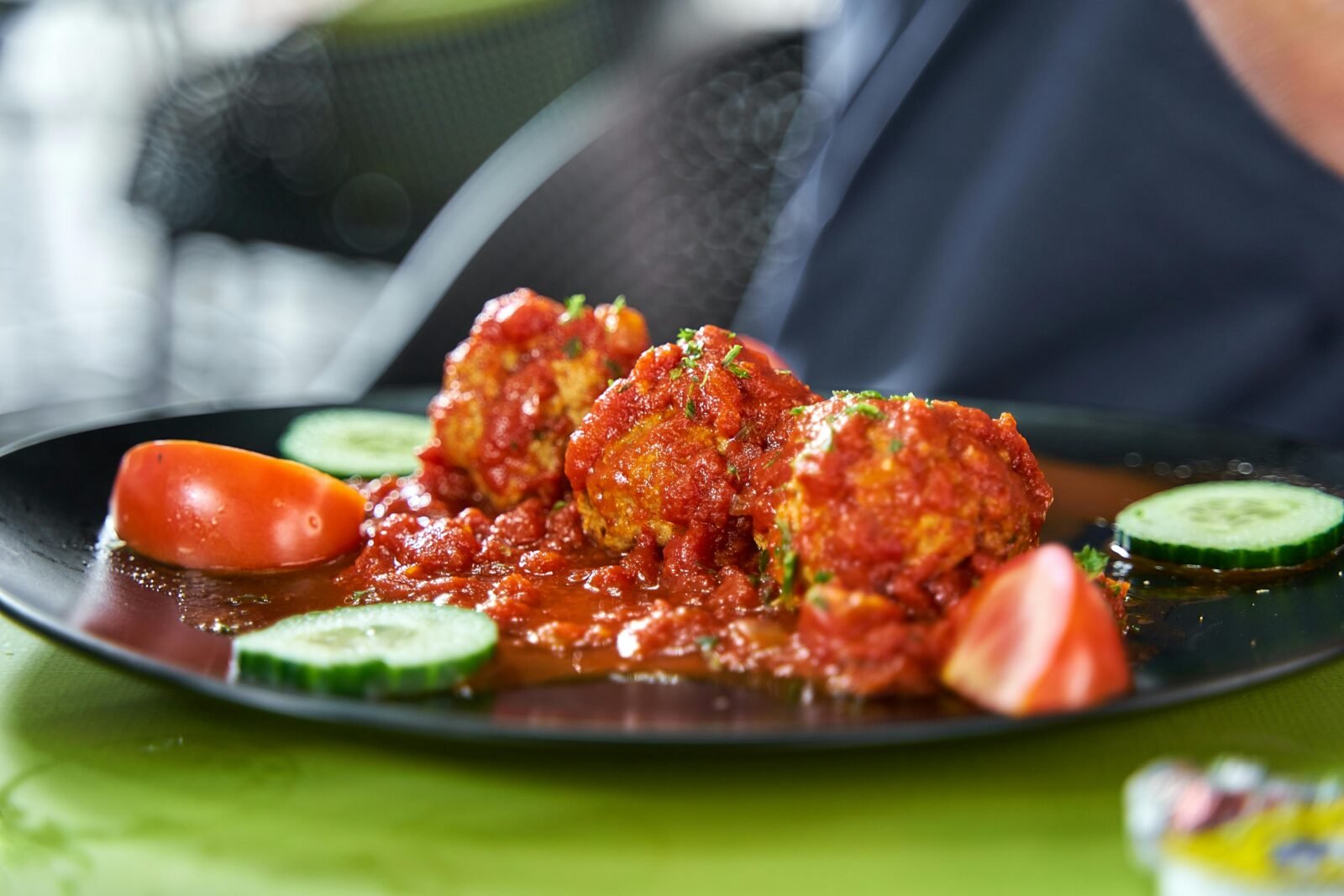 Albóndigas caseras en salsa de tomate servidas en plato negro con pepino y tomate