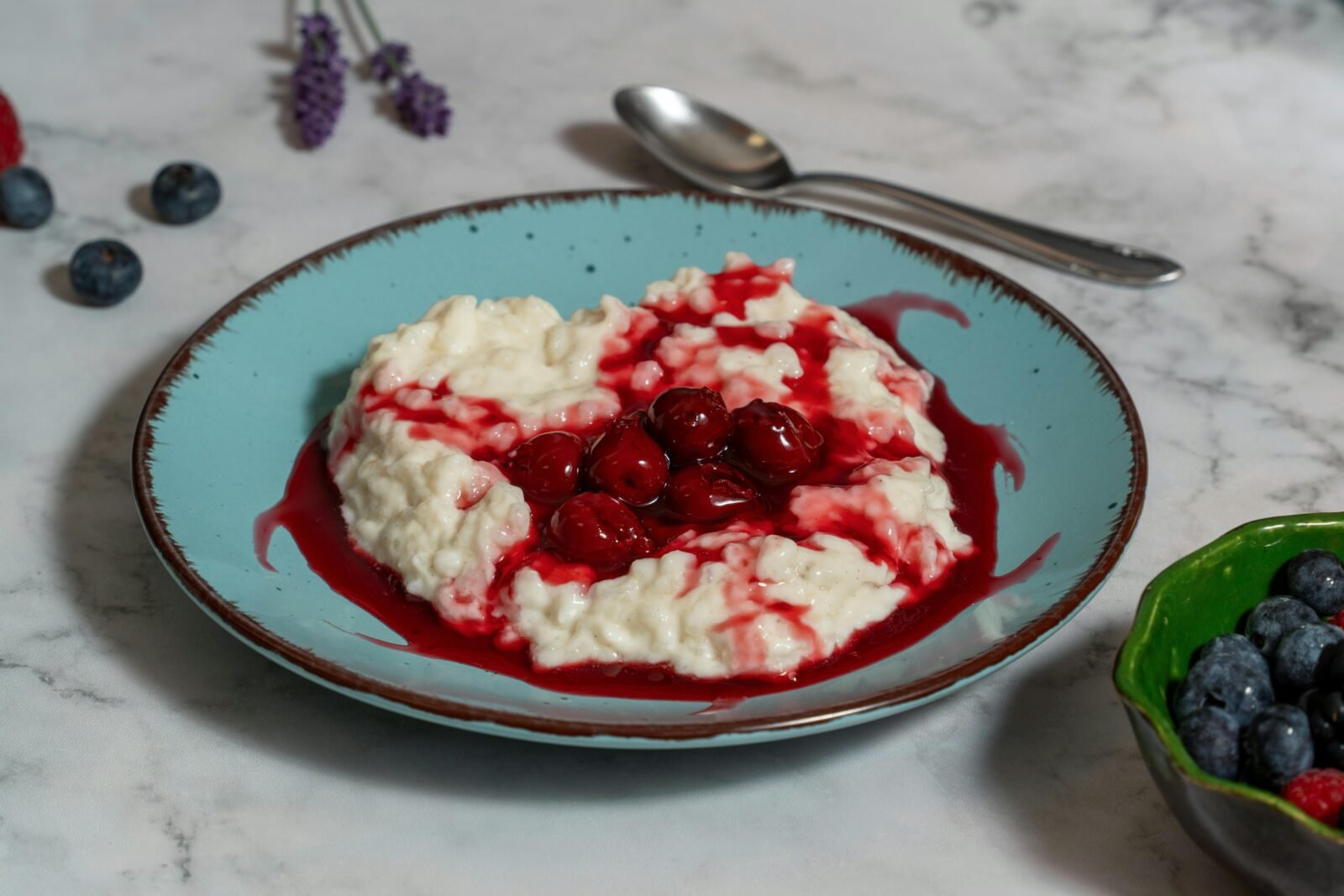 Creamy rice pudding topped with juicy cherries on a blue plate.