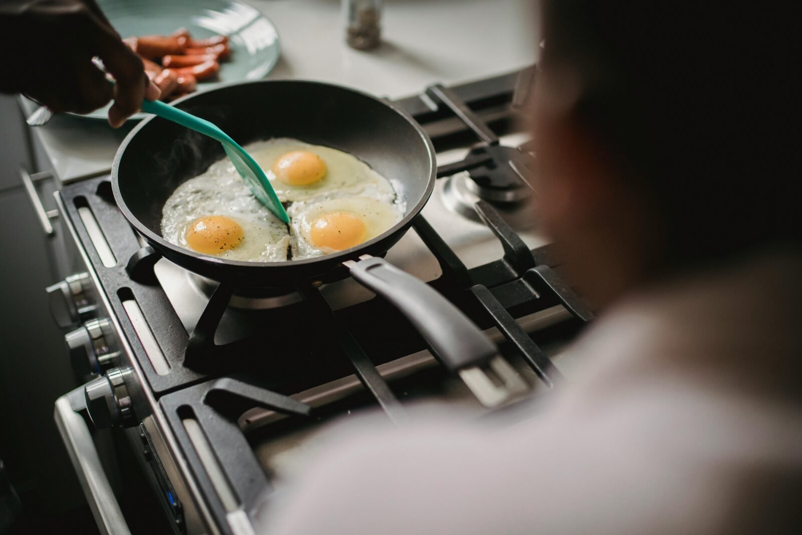 A person prepares fried eggs on a stove for breakfast, emphasizing home cooking and food preparation.
