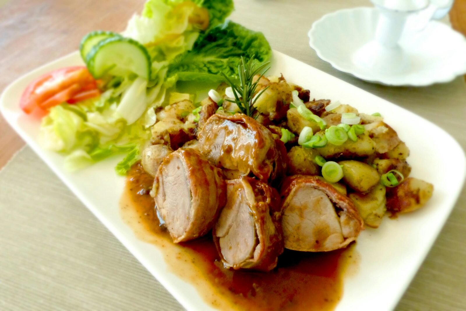 Delicious pork tenderloin garnished with rosemary, served with roasted potatoes and fresh salad.